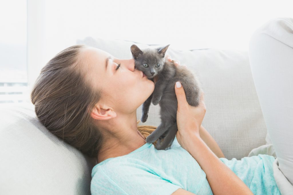 Veselá žena leží na pohovke a bozkáva sivé mačiatko